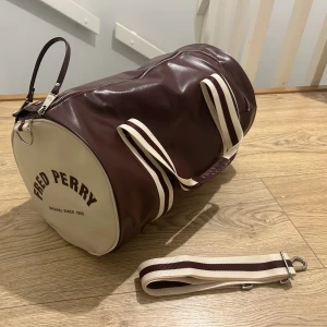 Fred perry väska - Fred Perry barrel bag. Knappt använd så den är i nyskick. Den är äkta, köpt ifrån fred perrys officiella.