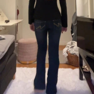 Mörkblå bootcut jeans från Nelly - Mörkblå jeans från Nelly med bootcut passform och snygga kontrastsömmar. Bakfickorna har coolt broderad zigzag-detalj i gul 