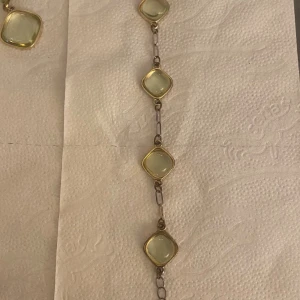 Armband med ljusgröna stenar och guldkant  - Unikt armband med fyrkantiga ljusgröna stenar infattade i guldfärgade ramar. Stenarna är länkade med tunna metallkedjor som ger ett stilrent och elegant intryck. Perfekt för dig som gillar smycken med en modern och fräsch vibe.