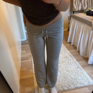 Stickade mjukisbyxor med snörning - Gråa stickade lågmidjade mjukisbyxor med ribbad midja och snörning. Från Gina Young så strl 146/152. Korta på mig som är 158cm. Aldrig använda, fick i present. Byxorna har en rak passform, perfekta för en chill och avslappnad stil.