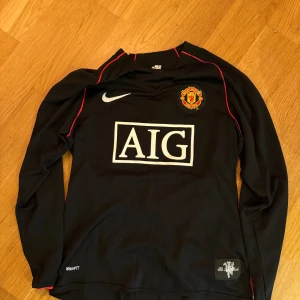 Manchester United långärmad Ronaldo-tröja - Säljer en svart långärmad Manchester United fotbollströja från Nike med röda detaljer. Tröjan har AIG som sponsor på bröstet, klubbmärke, och Ronaldo 7-tryck på ryggen. Tillverkad i NikeFIT Dry-material som andas och passar perfekt för fotbollsträning.