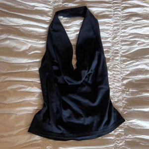 Mörkblå halterneck topp i - Säljer en mörkblå halterneck topp i glansigt  material. Toppen har djup v-ringning och är ärmlös med en snygg draperad effekt framtill🩷