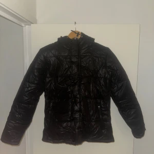 Svart pufferjacka med randig huva - Ny vinterjacka / puffer jacka Helt ny jacka, aldrig använd. Endast uppackad ur kartongen. Svart pufferjacka med luva (randigt foder). Lite skrynklig efter att ha legat i kartong. Passar barn/ungdom ca 9–11 år.  Pris: 300 kr pris kan diskuteras vid snabb affär