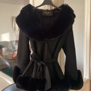 Svart pälsjacka från Giorgia Fashion  - Snygg svart pälsjacka från Giorgia Fashion i storlek S/M storleken XL är fel. Jackan har stora fluffiga pälskanter vid krage, ärmslut och nederkant samt ett bälte i midjan för extra snygg siluett. Perfekt för dig som vill sticka ut med en lyxig och trendig look under vinter och hösten.