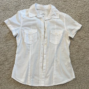 Vit kortärmad skjorta från H&M - Snygg vit skjorta från H&M L.O.G.G med korta ärmar och klassisk krage. Skjortan har två bröstfickor med knappar och är tillverkad i 100% bomull. 
