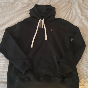 Svart hoodie från Polo Ralph Lauren - Svart hoodie från Polo Ralph Lauren i storlek L . Säljer då de blev fel storlek när jag köpte. Helt ny med lapparna kvar