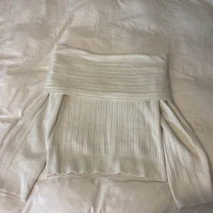 Offshoulder ribbad stickad tröja - Snygg offshoulder tröja i vitt stickat material med ribbad struktur. Toppen har långa ärmar och en bred kant upptill.
