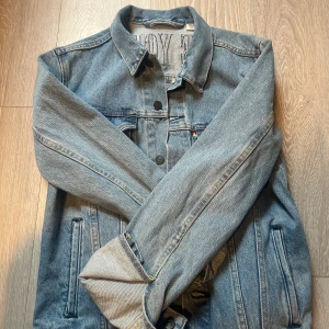 Klassisk blå jeansjacka från Levi's - Säljer en klassisk blå jeansjacka från Levi's med raka linjer, bröstfickor med lock och knappar framtill. Jackan har en avslappnad passform och är tillverkad i slitstarkt denim. Perfekt för dig som gillar tidlös streetstyle.