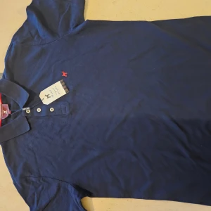 Marinblå henley från Williot - Snygg marinblå henley från Williot med klassisk krage och tre vita knappar framtill. Skjortan har ett litet rött broderat hundmotiv på bröstet och är tillverkad i mjuk bomull. Perfekt för dig som gillar stilrena och bekväma plagg med en cool detalj.