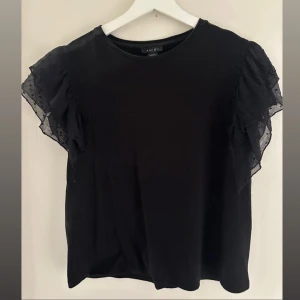 Svart blus med volangärmar  - Så fin blus med korta volangärmar i transparent tyg och diskret prickigt mönster. Använd sparsamt och i mycket bra skick! 