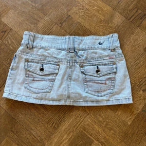 Ljusblå mini jeanskjol - Superfin ljusblå jeanskjol med dubbla knappar framtill, bakfickor med knappdetaljer. Den är lågmidjad.