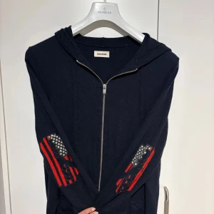 100% Kashmir hoodie från Zadig & Voltaire - Svart hoodie med dragkedja från Zadig & Voltaire. Tröjan har huva och detaljerade mönster i rött, vitt och blått på ärmarna. Skit ball tröja som jag råka krympa i tvätten och gick från en storlek L till M/S.😩