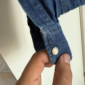 Jeansskjorta från Lee, slim fit M - Snygg jeansskjorta från Lee i klassisk blå denim. Slim fit-modell med långa ärmar, tryckknappar och två bröstfickor med lock. Perfekt för dig som gillar en tidlös och cool look. Materialet är tåligt jeans och skjortan har Lee-logga på bröstet.