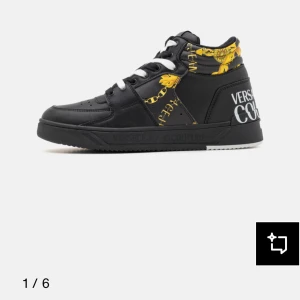 Versace Jeans Couture svarta sneakers - Svarta sneakers från Versace Jeans Couture med vita snören och detaljer i gult barockmönster. Skorna har en högre siluett, rund tå och platt sula. Märkeslogga syns tydligt på hälen och sidan. Tillverkade i syntetmaterial med lyxig känsla och unika detaljer.
