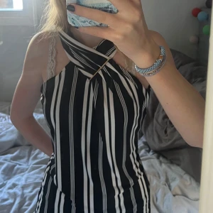 Svartvit randig klänning Calvin Klein - Snygg svartvit randig klänning från Calvin Klein med cool omlottkrage och guldfärgad detalj framtill. Klänningen är ärmlös och har dragkedja i ryggen. ALDRIG ANVÄND!