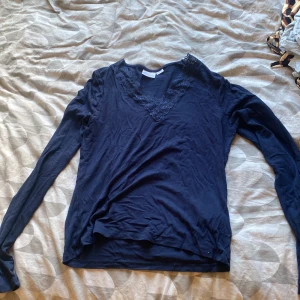 Mörkblå långärmad topp med spets - Mörkblå långärmad topp från Gina Tricot med snygg v-ringning och spetsdetaljer runt halsen. Tunn och mjuk, perfekt för lager-på-lager eller som den är. Enkel att matcha med både jeans och kjol.