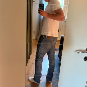 Blå jeans från Denim & Supply Ralph Lauren - Säljer ett par klassiska blå jeans från Denim & Supply Ralph Lauren. Jeansen har en rak passform, normal midja och snygga slitningar för en avslappnad look. Detalj med amerikansk flagga vid myntfickan och läderpatch bak i midjan. Priset är inte hugget i sten