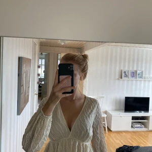 Vit omlottblus med struktur från SHEIN - Supersöt vit omlottblus från SHEIN i storlek S. Blusen har v-ringning, långärmade puffiga ärmar och ett strukturerat mönster i tyget. Den har en lätt volang nertill och markerad midja som ger en romantisk vibe.