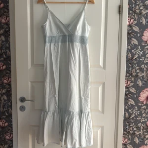 Ljusblå långklänning med volang - Superfin ljusblå långklänning med smala axelband och omlott-v-ringning.