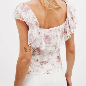 NA-KD Blommig spetsblus med volang - Supersöt blus i vitt med rosa blommigt mönster och volangdetaljer över axlarna. Storlek S men passar allt den Xs-S. Perfekt för dig som gillar en feminin och somrig stil. Den är ny med prislapp. 