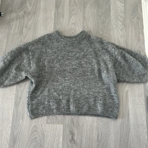 Grå stickad tröja från Gina Tricot - Mysig grå stickad tröja från Gina Tricot i oversized modell. Tröjan har rund halsringning, långa ärmar och ribbade muddar vid hals, ärmslut och nederkant. Perfekt för lager-på-lager och chill dagar. Ej använd. 