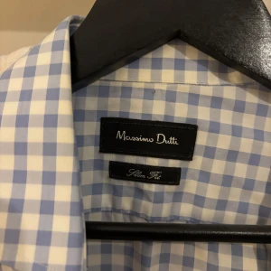 Blårutig skjorta från Massimo Dutti - Snygg blårutig skjorta från Massimo Dutti i slim fit-modell. Skjortan har klassisk krage, långa ärmar och knäppning framtill. Tillverkad i mjuk bomull som känns skön mot huden. Perfekt för dig som gillar stilrena och fräscha plagg.