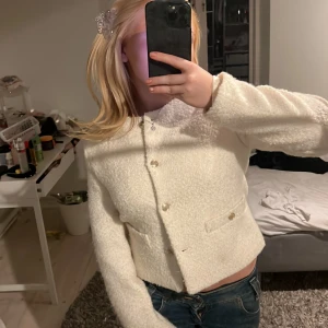 Vit bouclé-kofta med guldknappar - Säljer en superfin vit kofta i bouclé-liknande material med snygga guldknappar framtill. Kortare modell med två fickor och lång ärm. Perfekt att styla med jeans eller kjol för en chic look.
