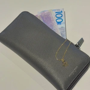 Grå plånbok Michael Kors skinn - Snygg grå plånbok från Michael Kors i strukturerat skinn med silverfärgad dragkedja. Plånboken har flera kortfack, myntfack med dragkedja och plats för sedlar. Perfekt för dig som vill ha stilren och lyxig känsla i vardagen.