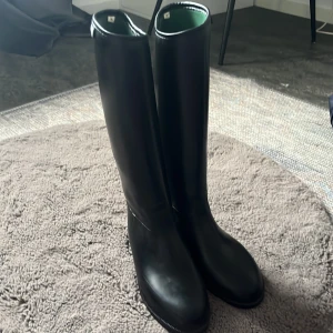 Svarta höga stövlar från Crw, strl 35 hööks - Snygga svarta höga stövlar från Criv i storlek 35. Klassisk och stilren design med rund tå och platt sula. Utsidan är i syntetmaterial och insidan har en grön textil. Perfekta för dig som vill ha en clean look till höst och vinter. Använd fåtal ggr
