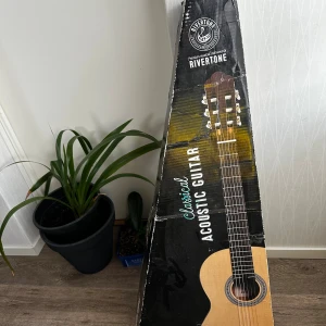 Rivertone Classical Acoustic Guitar - Klassisk akustisk gitarr från Rivertone i mycket fint skick. Levereras i originalkartong. Vacker träfinish, nylonsträngar och traditionell design. Inga synliga repor eller skador, perfekt för nybörjare och entusiaster.