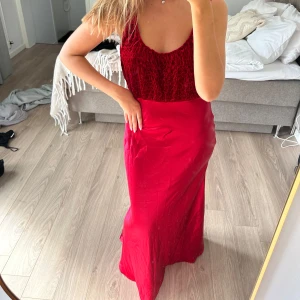 Röd långklänning från Byoung - Snygg röd långklänning från Byoung med smala axelband och figurnära passform. Överdelen är i ett strukturerat, stretchigt tyg och kjolen är i glansigt, slätt material. Perfekt för dig som vill sticka ut med en elegant look. Klänningen följer kroppen på ett så smickrande sätt! 