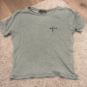 Ribbad grön topp från Primark XS - Säljer en ribbad ljusgrön topp från Primark i storlek XS. Toppen har korta ärmar, rund halsringning och ett litet svart tryck med texten 'live more' på bröstet. Perfekt för en chill och avslappnad stil.