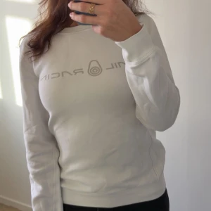 Vit Sail Racing Tröja - Vit sweatshirt från Sail Racing med grått tryck på bröstet. Tröjan har rund hals, långa ärmar och ribbade muddar vid ärmslut och nederkant. Mjuk och skön bomullskvalitet, perfekt för chill dagar. Snygg och enkel design med logga framtill. 🤍