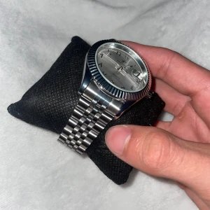 Silverfärgad klocka från Riceco - Stilren klocka från Riceco med silverfärgad urtavla och arabiska siffror. Klockan har en klassisk rund form, räfflad bezel och länkarmband i metall. Urtavlan har datumfönster och quartz-urverk. Perfekt accessoar för dig som gillar en clean och modern look.