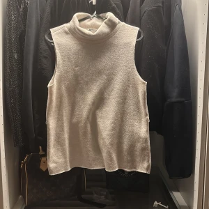 Beige ärmlös polotopp från Zara - Beige ärmlös polotopp från Zara i mjukt, strukturerat material. Toppen har hög krage och en rak, avslappnad passform som ger en clean och stilren look. Perfekt att styla med jeans eller kjol för en trendig vibe.