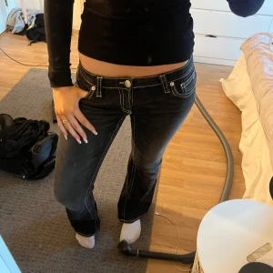 Svarta bootcut jeans med kontrastsömmar - Säljer ett par svarta jeans med tydliga vita kontrastsömmar och snygg broderad detalj på bakfickorna. Modellen är lågmidjad och har bootcut-ben, vilket ger en schysst siluett. Från 14+ Gina avdelningen i storlek M men sitter bra på mig som bär S