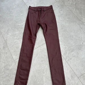 Vinröda skinny jeans från Dr Denim - Snygga skinny jeans med skinnlook från Dr Denim. I höstens färg vinrött. Byxorna är tillverkade i en mjuk blandning av rayon, nylon och spandex som ger en skön stretchig känsla. Storlek M. 