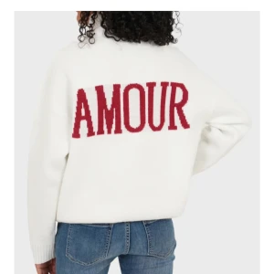 Vit polotröja med röd AMOUR-text - Vit stickad polotröja med hög krage och breda muddar. På ryggen står det AMOUR i stora röda bokstäver. Tröjan har en loose passform och är parfekt nu till hösten. Från Meet me there helt ny med lappen på då den var förstor på mig❤️