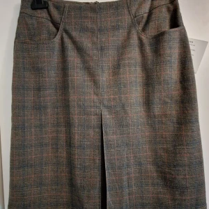 Grå knälångkjol med diskret rutmönster - Snygg knälångkjol i grått med svagt rutigt mönster.. Kjolen har en klassisk rak passform, slits framtill och baktill samt två fickor. Ej använd.