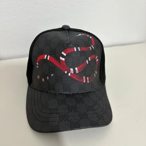 Svart GG keps - En snygg svart GG keps med ormtryck. Är helt ny och oanvänd. 