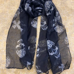  halsduk med döskallemönster och kors  - Snygg  halsduk med coola vita döskallar och kors som mönster. Halsduken är tunn och luftig, perfekt att slänga över axlarna för en edgy vibe. Materialet känns lätt och skönt mot huden, och den passar grymt till både jacka och t-shirt.