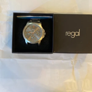 Silverfärgad klocka från Regal - Stilren klocka från Regal med rund urtavla i grått och detaljer i silver och koppar. Klockan har tre mindre urtavlor och ett klassiskt armband i metall. Perfekt accessoar för dig som gillar en clean och modern look.