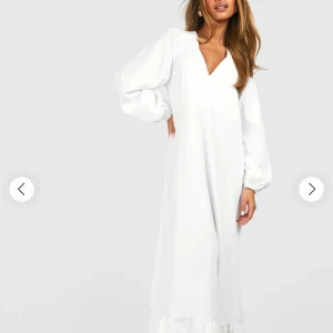 Vit långklänning med v-ringning - Vit långklänning med v-ringad hals och puffiga långärmar. Klänningen har en loose passform och volangdetalj längst ner. Perfekt för dig som gillar en enkel men stilren look. Materialet ser ut att vara bomull eller polyester.