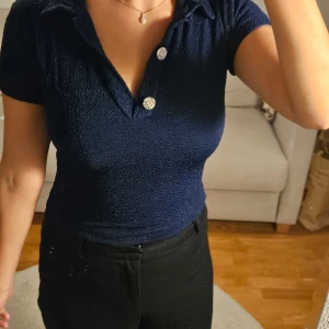 Marinblå topp från Mexiko - Säljer en marinblå polotopp med korta ärmar och dekorativa knappar framtill. Toppen har en krage och är gjord i ett frottéliknande material. Inköpt i Mexiko. Skulle säga att den passar storlek XS-S 