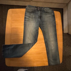 Blå jeans Jack & Jones Regular Clark - Snygga blå jeans från Jack & Jones i modellen Regular Clark. Klassisk femficksdesign med normal passform och raka ben. Jeansen har en tvättad look med ljusare partier och är tillverkade i slitstarkt denimtyg. Perfekta för en avslappnad stil. Storlek 29/30