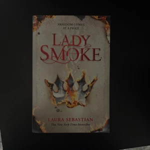 Lady Smoke - En spännande bok med en brinnande krona på omslaget och texten 'Freedom comes at a price'. Perfekt för dig som gillar episka berättelser och dramatik. Skriven av New York Times-bästsäljaren Laura Sebastian.