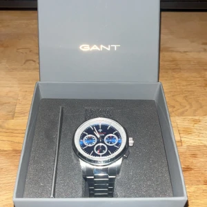 GANT herrklocka med blå urtavla - Stilren herrklocka från GANT med blå urtavla och tre mindre kronografer. Boetten och armbandet är i silverfärgat metall, och klockan levereras i originalask med extra länkar och ett brunt fodral. Perfekt accessoar för dig som gillar klassisk design med sportig touch.