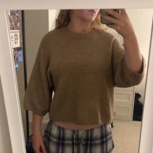 Beige stickad croppad tröja - Mysig beige stickad tröja med croppad passform och trekvartsärmar. Perfekt för lager-på-lager och chill dagar. Enkel design med rund halsringning och mjukt material.