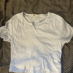Ljusblå topp från FB Sister - Säljer en ljusblå topp från FB Sister i storlek M. Toppen har korta ärmar, v-ringad hals med liten slits och är tillverkad i mjuk bomull. Enkel och fräsch design som är lätt att matcha med dina favoritjeans eller kjol.