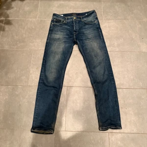 Jack & Jones blå tapered jeans strl 30/30 - Snygga blå jeans från Jack & Jones i modellen Tapered Mike. Jeansen har klassisk femficksdesign, gul kontrastsöm och en något avsmalnande passform. Perfekt för dig som gillar en modern och avslappnad stil.